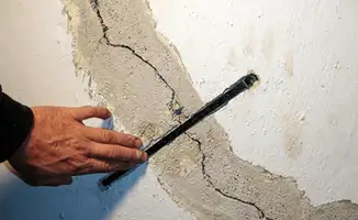 A wall with a large crack is being inspected by a professional in Charlotte, NC
